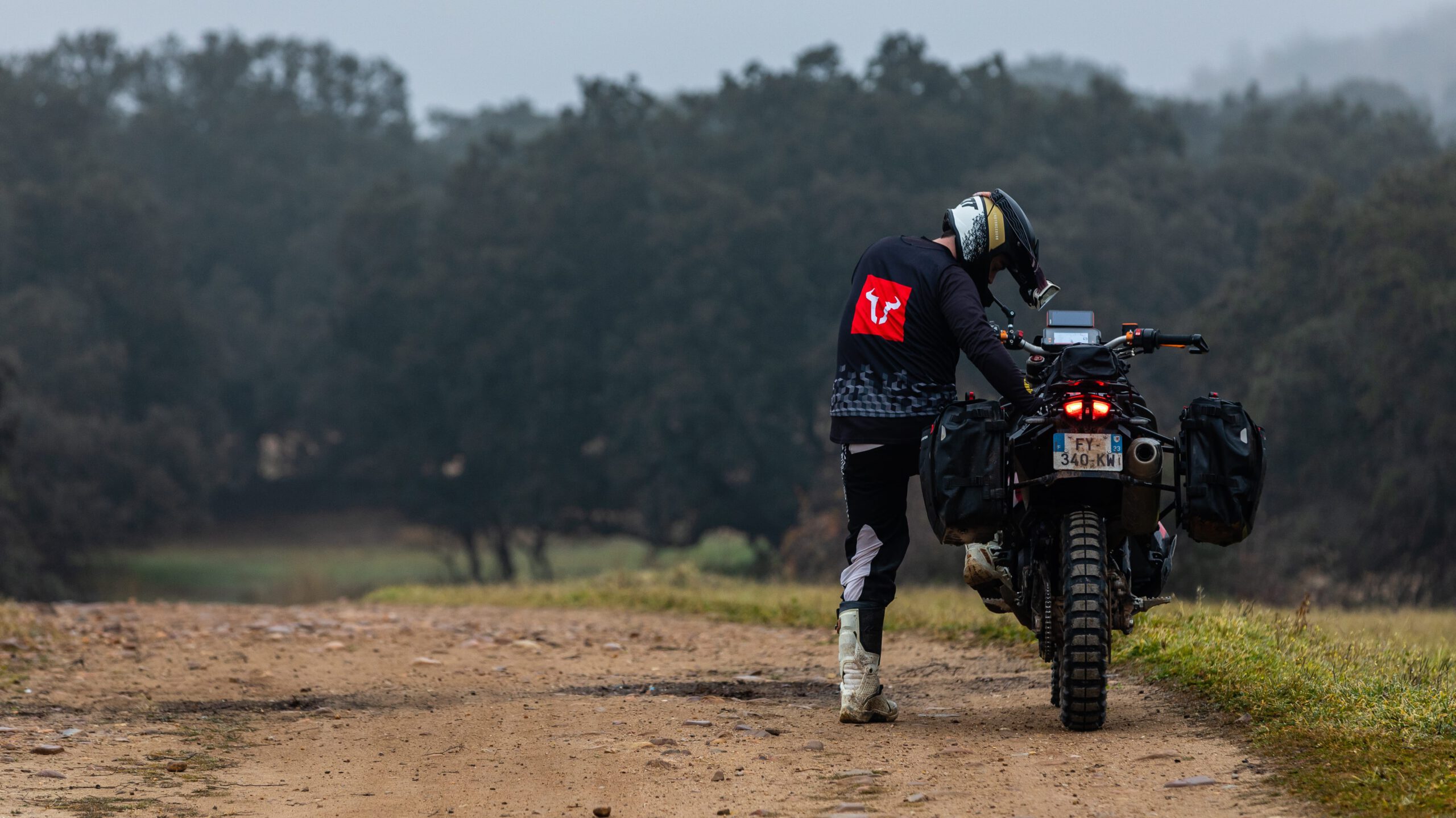 Motorista revisando su KTM 890 Rally equipada con maletas Sysbag WP de SW-Motech en un camino rural